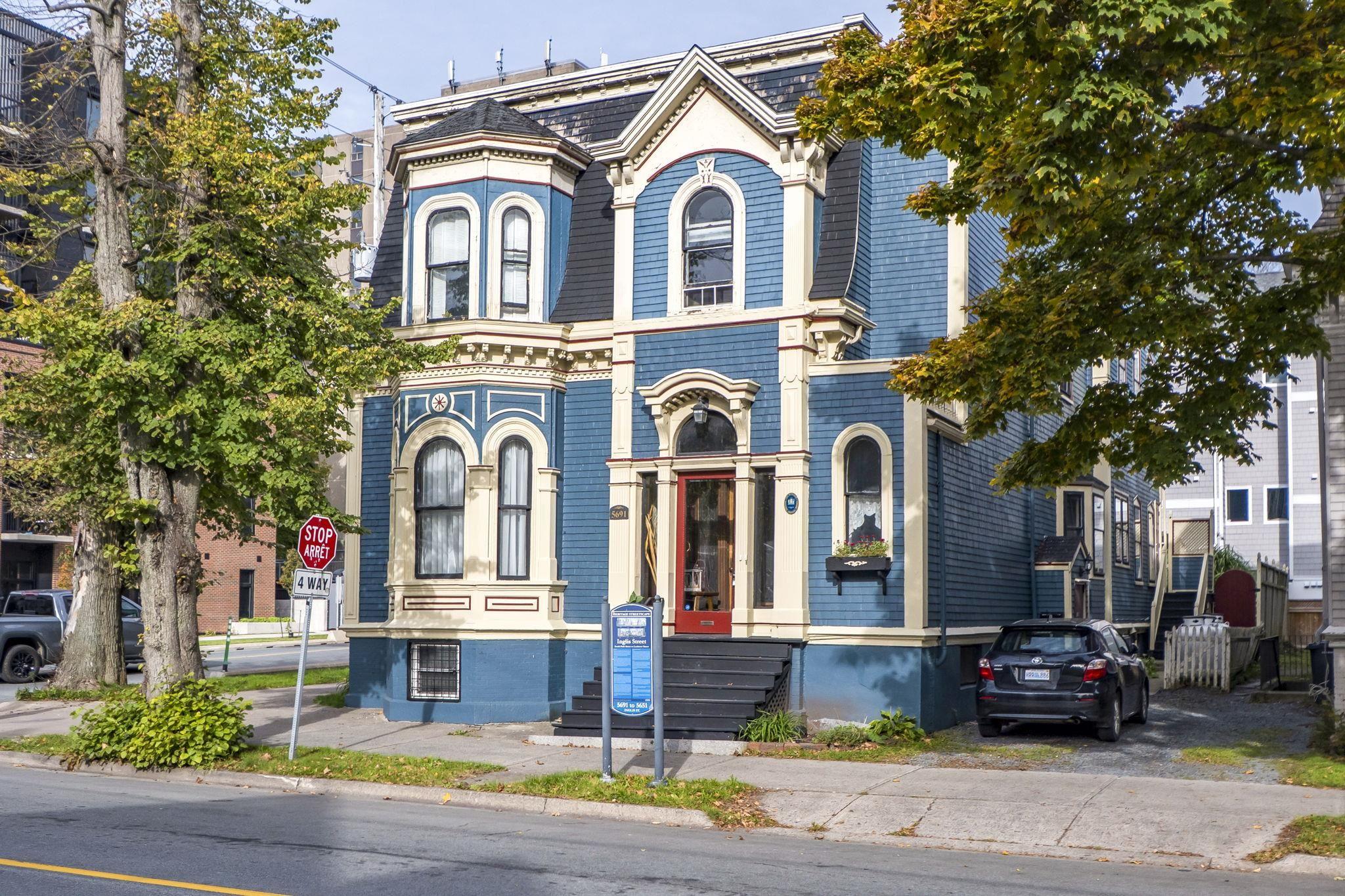 Victorian-style exterior featuring patterned wood shingle siding, a prominent mansard roof, intricate decorative trim, a bay window, and a central entryway with transom glass