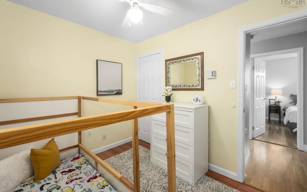 Room featuring pale yellow walls, wood-finish flooring, a white ceiling fan with integrated lighting, and a white six-drawer dresser