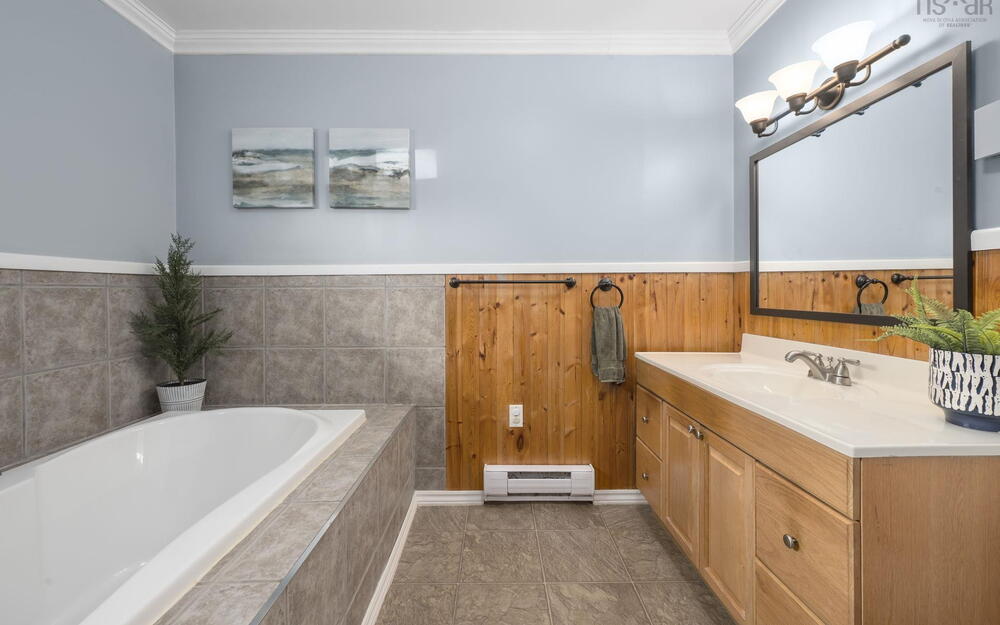 Bathroom featuring a built-in tub with tile surround, a wood-finish vanity with an integrated sink, a rectangular framed mirror, and a three-light vanity fixture