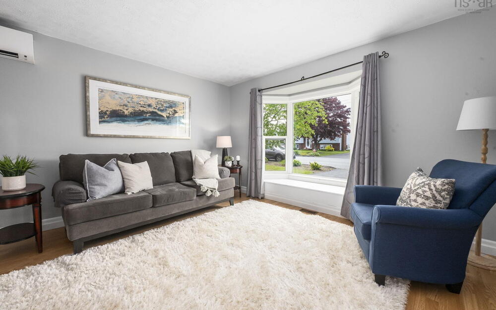 Bright living space with light-toned walls, wood-finish flooring, and a large bay window