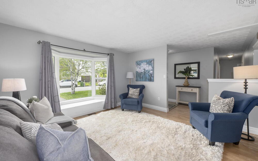 Living area featuring light wood-finish flooring, a large bay window with a built-in window seat, light gray wall paint, and a textured white ceiling
