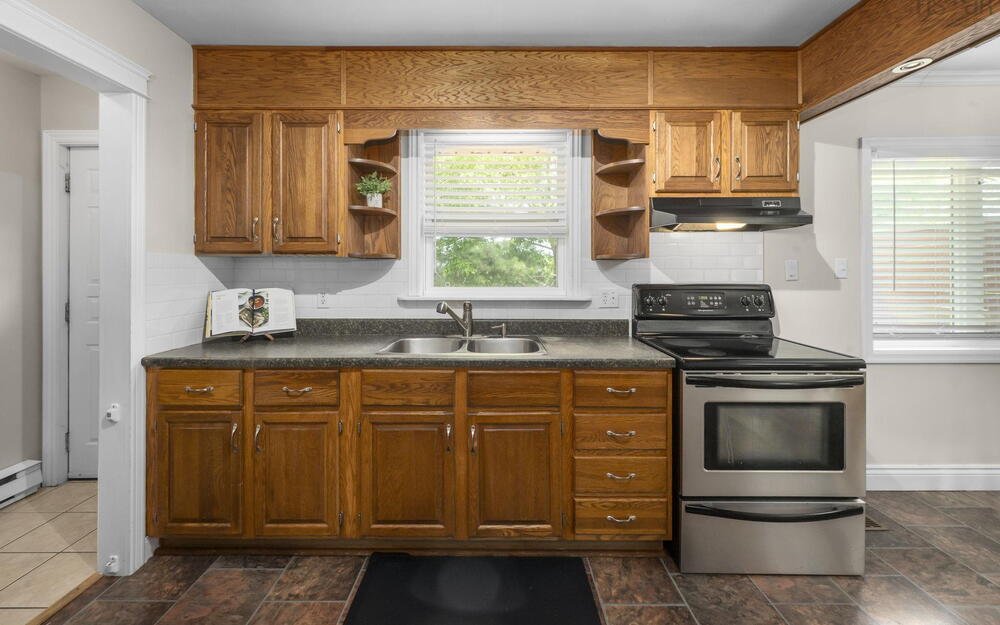 Kitchen featuring wood cabinetry, stainless steel oven, dual basin sink, white subway tile backsplash, and dark laminate countertops