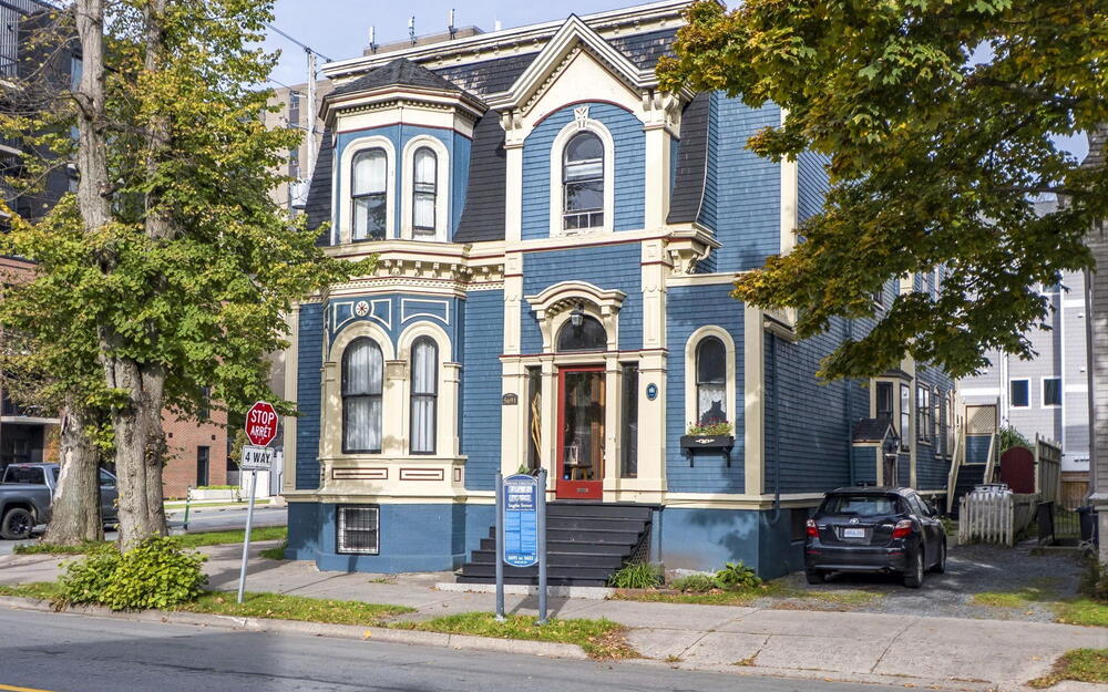 Victorian-style exterior featuring patterned wood shingle siding, a prominent mansard roof, intricate decorative trim, a bay window, and a central entryway with transom glass