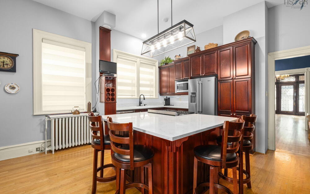 Kitchen featuring a central island with a stone-finish countertop, custom cherry-toned cabinetry, stainless steel appliances, wood-finish flooring, and a linear pendant light fixture
