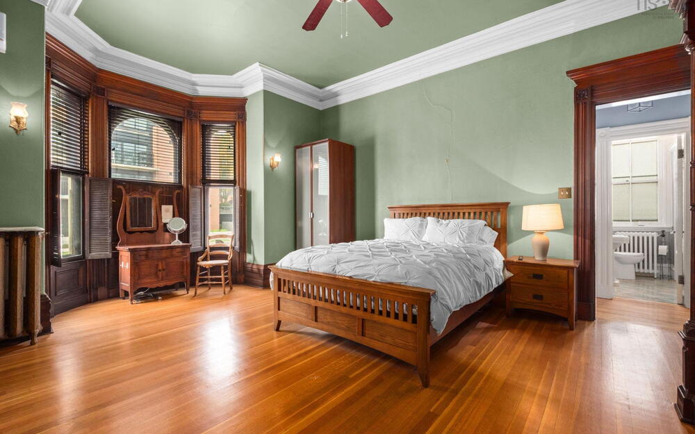 Room featuring original wood-finish flooring, ornate millwork, bay windows with integrated shutters, and crown molding