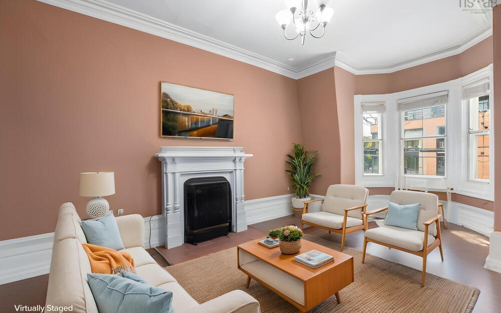 Living room featuring a prominent fireplace with a classic mantel, bay window, crown molding, and wood-finish flooring