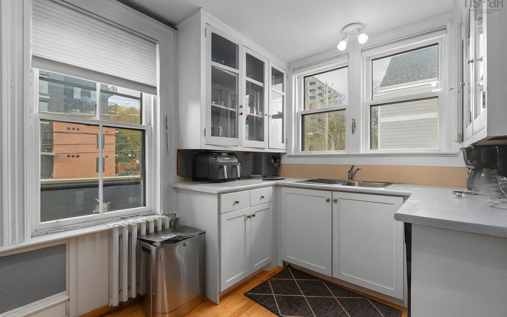 Kitchen featuring shaker-style cabinetry with glass-front uppers, solid-surface countertops, dual-basin stainless steel sink, and wood-finish flooring