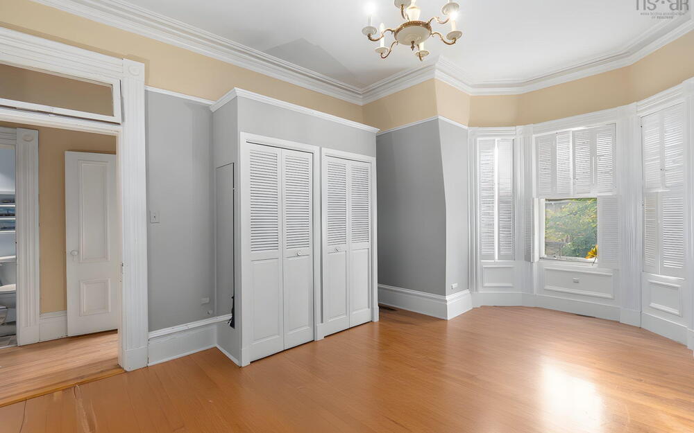 Bay window with white trim, wood-finish flooring, built-in louvered-door closets, crown molding, and tiered ceiling
