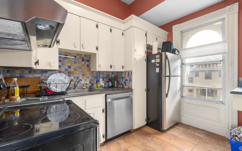 Kitchen featuring white cabinetry, mosaic tile backsplash, stainless steel appliances, tile flooring, and arched window detailing