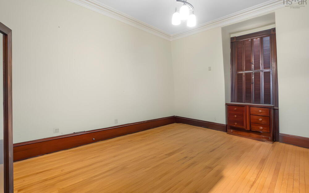 Hardwood flooring, natural wood trim, built-in cabinetry, recessed window area with shutter accents, and crown molding