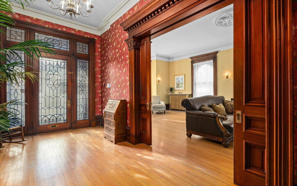 Entryway featuring natural wood-finish flooring, ornate woodwork, custom leaded glass door panels, intricate crown molding, and a built-in ceiling medallion