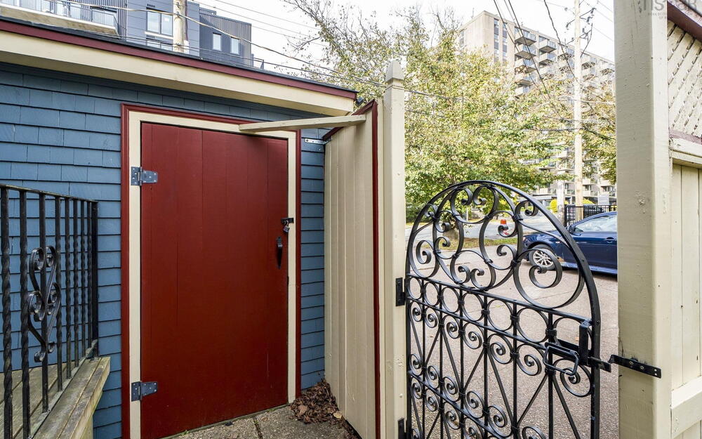 Exterior entrance featuring blue shingle siding, a red solid-core door with metal hinges, and a decorative wrought iron gate mounted to a perimeter fence
