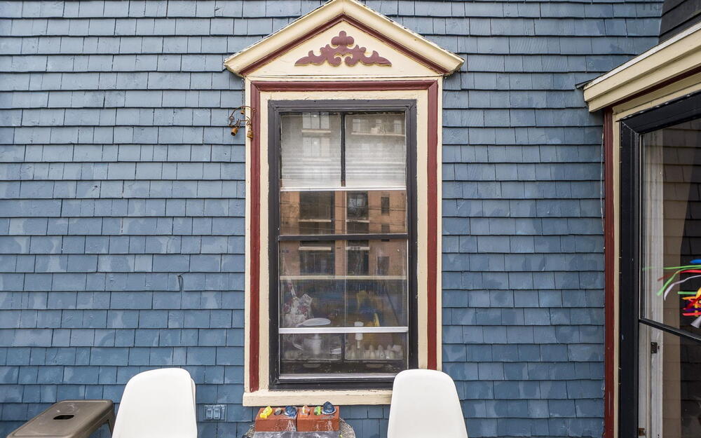 Exterior wall featuring blue shingle siding and a vertical window with a decorative arched pediment and multi-toned trim