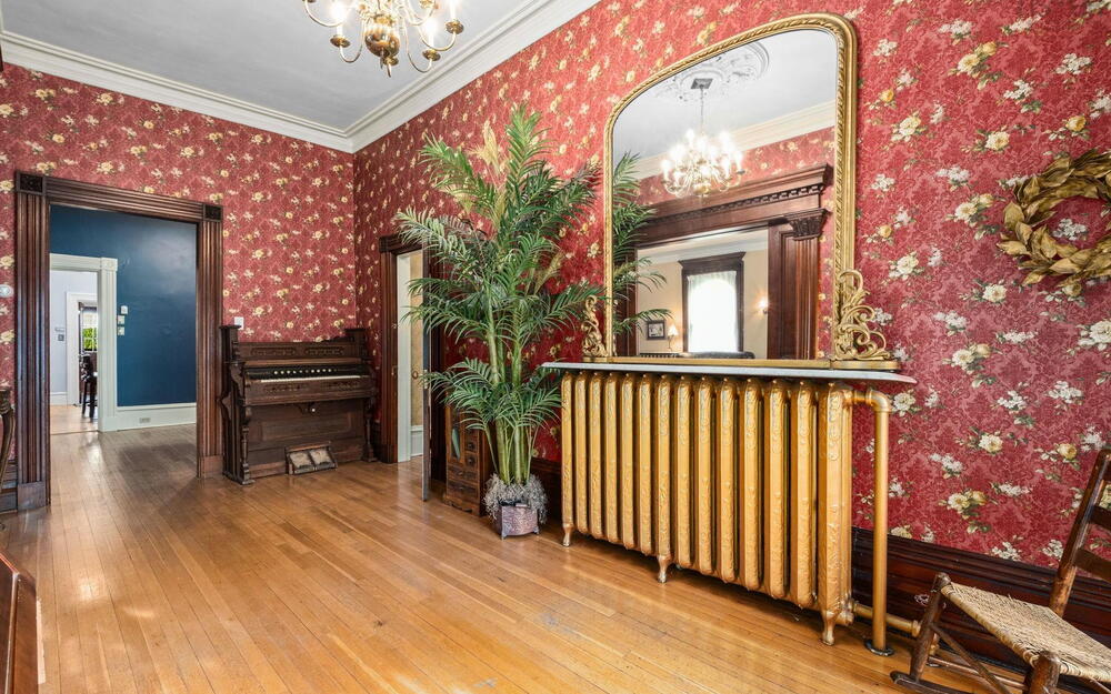 Hardwood flooring, ornate wood door casings, vintage-style metal radiator with a stone-top console, ceiling medallion, and decorative multi-arm chandelier